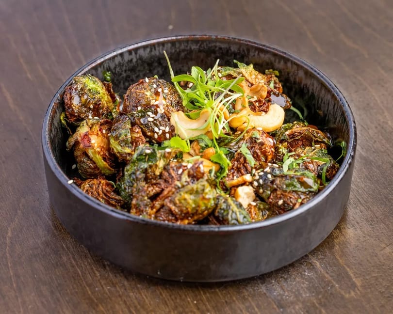 Roasted Brussels sprouts with cashews, sesame seeds, and microgreens in a dark bowl.