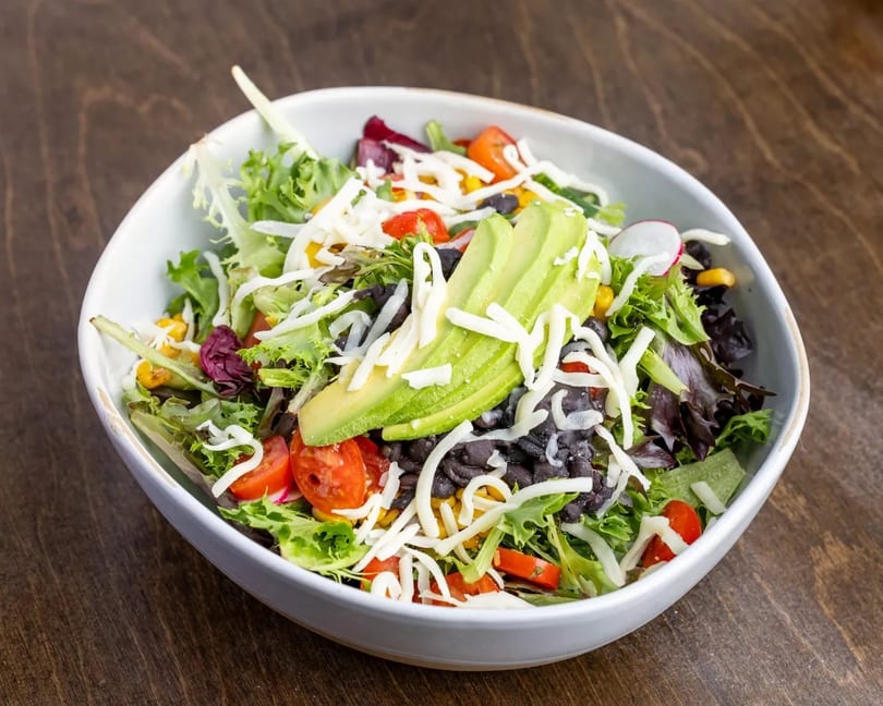 Fresh salad with mixed greens, black beans, corn, cherry tomatoes, avocado, and shredded cheese.