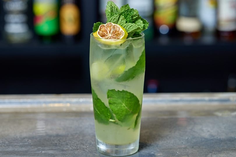 Refreshing mojito cocktail with mint leaves and a dried lime slice on a bar counter.